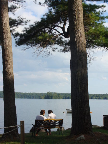 Kippewa campers on a bench under trees overlooking lake cobbosseecontee