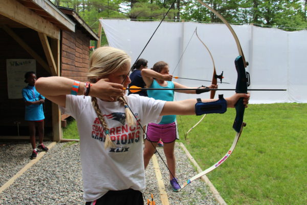 girl learning archery with a bow and arrow at Camp Kippewa